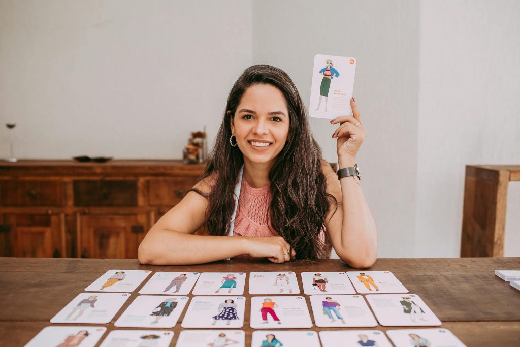 Woman with long hair smiling and holding educational flashcards while seated indoors.
